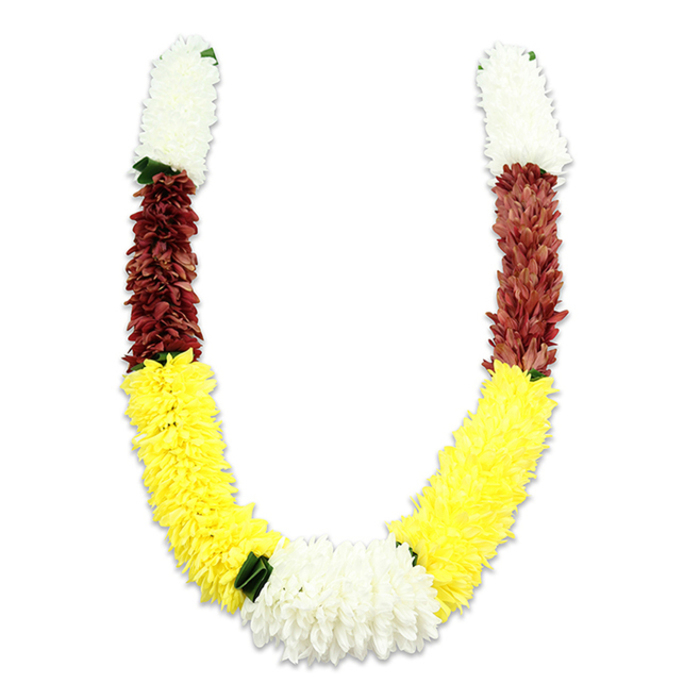 A richly coloured, handcrafted U-shaped mala is presented on a bright white background, its clean shadow suggesting soft, directional studio light and careful staging. From each top end the garland opens with a dense, cylindrical segment of creamy-white tiny petals that read like miniature chrysanthemum or jasmine clusters - airy yet compact, with a fluffy texture that invites the eye to linger. Beneath each white cap a band of maroon or deep reddish-brown follows, the tiny, fabric-like petals packed tightly to form a velvety midsection. The design then flows into the longest, most exuberant portion: a ribbon of vivid yellow that shapes the generous U-curve, each yellow element sculpted to resemble marigold-like fullness. At the curve's deepest point a larger cluster of pure white chrysanthemum-style blooms unites the two arms, providing a luminous centrepiece framed by intermittent dark-green leaf accents that separate colour blocks and add structural contrast. The construction reveals expert floral handiwork - thousands of individual synthetic petals layered to achieve natural movement and volume while ensuring durability for repeated ceremonial use. In the Bexleyheath community these garlands are familiar at Hindu pujas, wedding mandaps, and festival altars in venues around The Broadway and near Crook Log, where cultural celebrations bring neighbours together. Crafted by local hands and often reproduced by Flower Delivery Bexleyheath for cultural décor, the piece balances tradition and practical longevity, its colours signalling purity, prosperity, and devotion in a tactile, visual language that resonates across local ceremonies and domestic shrines.