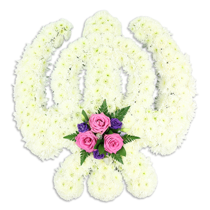The image shows a striking Sikh Khanda floral tribute, meticulously shaped and fully framed against a pristine white background so that every petal and contour can be appreciated. The sacred emblem is built entirely from tightly clustered white chrysanthemum florets, their small, ruffled petals overlapping to form a plush, continuous surface. The central double-edged sword rises vertically, perfectly straight, encircled by the smooth ring of the chakkar, while the two kirpans curve outwards from the base with a gentle, protective sweep. The crisp white blooms, evenly lit, give off a feeling of quiet radiance, symbolising purity, peace, and spiritual strength-qualities often sought in funeral tributes by Sikh families around Bexleyheath's diverse community. At the lower centre of the design, where the kirpans approach one another, a luminous accent arrangement adds warmth and personality. Three fresh pink roses sit proudly at the heart of this cluster, their petals tenderly furled as though in mid-blossom. Around them, smaller deep purple flowers, perhaps freesias or similar, introduce a rich jewel tone that deepens the emotional resonance of the piece. Wisps of dark green fern and foliage weave between the blooms, lending texture and a sense of natural movement, as if a small garden has been tucked carefully into the base of the Khanda. A faint shadow beneath the tribute grounds it gently, suggesting it rests on a tabletop in a quiet farewell setting. This bespoke arrangement, ideal for Sikh funerals, memorial services, or commemorations in and around Bexleyheath-from local gurdwaras to family homes-serves as a thoughtful floral testament to love, honour, and enduring faith.