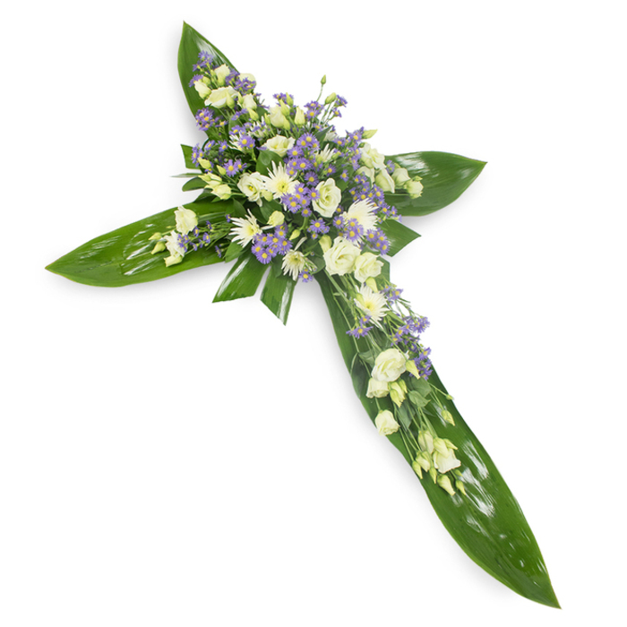 This poignant floral cross reads like a quiet hymn in foliage and blossom, carefully arranged on a plain white surface and shot from a gentle overhead angle to reveal its layered craftsmanship. A foundation of wide, waxy green tropical leaves-their veins and glossy texture plainly visible-creates the unmistakable shape of the cross, the leaves overlapped so the arms are defined and held with a natural strength. At the centre and extending outward along each arm, clusters of pale, ruffled lisianthus in soft white and creamy ivory form the heart of the composition; their tender, layered petals suggest refuge. Intermingled are compact white chrysanthemum-type blooms that add small, bright points of calm, and wisps of lavender-toned, star-like limonium or aster give the arrangement a delicate, cooling breath of colour. Slender green filler threads through the blooms, offering fine texture and a suggestion of movement, while the soft, even lighting gives the whole tribute a serene, luminous quality reminiscent of early morning light over Danson Park. The overall mood is one of composed remembrance and spiritual consolation-appropriate for funeral services, church gatherings, or graveside placements in the Bexleyheath area-where families seek a dignified, heartfelt way to honour a life. Tactile contrasts between the smooth, glossy foliage and the feathery petals create a visual balance that feels both steadfast and compassionate.