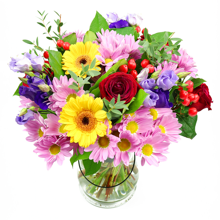 A richly coloured mixed bouquet stands tall in a clear glass vase, its shape rounded and abundant, with every bloom positioned against a clean white background so the colours appear almost luminous. Deep red roses form the emotional core of the arrangement, their velvety petals spiralling inward in tight, luxurious whorls that suggest love, admiration, or heartfelt thanks. Close by, two bold yellow gerbera daisies with dark brown-orange centres provide a radiant counterpoint, their flat, open faces beaming with a warmth that would cheer any Bexleyheath doorstep delivery. Surrounding these standout flowers, plentiful soft pink daisies and chrysanthemums are layered in clusters, their many fine petals and golden-yellow centres contributing a gentle, relaxed charm that softens the overall look. Threaded through this blush-coloured surround, graceful stems of purple and lavender lisianthus rise and curve, their bell-shaped flowers introducing cooler, more muted tones that add elegance and depth, like the quiet calm of a late afternoon near Danson House. Small clusters of shiny red hypericum berries sparkle among the petals, adding rounded shapes and a slightly playful, modern accent. A variety of greenery is woven throughout - broad, dark leaves create a supportive frame, while slimmer, light-green shoots and sprigs bring freshness and a natural, just-picked feeling, reminiscent of a walk through the green spaces dotted around Bexleyheath. The transparent vase allows the viewer to see the neatly trimmed stems standing in clear water, lined up with precision, highlighting the florist's practiced craftsmanship. The overall effect is joyful, uplifting, and versatile, a bouquet that would suit birthday celebrations, congratulations, or a comforting thinking of you message delivered across the local area.