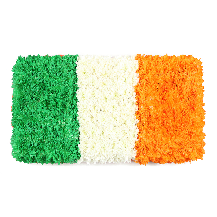 An elegant, rectangular floral arrangement replicates the Irish Tricolour, set against a stark white background. The flag is built entirely from thousands of small, densely packed petals, producing a textured, three-dimensional surface. From left to right: emerald green stripe composed of small petals (likely chrysanthemums or carnations) forming a plush field; central white stripe formed by tightly clustered white blooms; right orange stripe with petite orange florets. The white background makes the color blocks pop, and the overall rectangle mirrors the proportions of a state flag, with the tactile ridges and soft curves giving a handcrafted, intimate feel. The play of light across the petal surfaces adds depth, while the natural irregularities in surface texture highlight the artistry of the maker. The symbolism-the unity of tradition, lasting peace, and the celebration of Irish identity-lends the piece a ceremonial air. It works beautifully as a talking point in articles on Irish culture, St Patrick's Day, or heritage-focused displays, and is equally at home in event venues or shopfronts.In the local context of Bexleyheath, this poignant tribute can be found near The Broadway or in the shopping centre, a reminder of how floral art can carry meaning into everyday spaces. The flag's DNA-green for heritage, white for peace, orange for courage-resonates with families and community groups alike, making it a flexible centerpiece for weddings, parades, or community gatherings where expression of identity is celebrated.