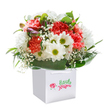 There's a sense of joyful anticipation in this bouquet, beautifully arranged and nestled in a crisp white gift bag-a familiar style seen in Bexleyheath's cherished florists. The coral and red carnations, lush and ruffled, fill the arrangement with warmth and exuberance, while fresh white daisies sparkle beside them, their yellow-green centers adding a cheerful brightness, like sunbeams over Bexleyheath's weekend fairs. Baby's breath peeks delicately between the main blooms, lending a gentle softness that feels light and sincere. Glossy, deep green foliage wraps the bouquet in a comforting embrace, its broad leaves reminiscent of shaded gardens along Bexleyheath's quieter streets. Among the flowers, several unopened buds-whispering shades of purple-hint at life's next turn, infusing the bouquet with depth and curiosity. The arrangement is finished with care in a white gift bag featuring sturdy ribbon handles, perfectly convenient for gifting across the local area or brightening someone's doorstep. Photographed sharply against a bright background, the bouquet's lush colours and artistic composition stand out, making it a thoughtful choice for birthdays, congratulatory moments, or simply for sharing the everyday beauty of Bexleyheath with someone special.